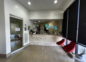 Dental office lobby — glass door, stone reception desk, red chairs, blue balloons