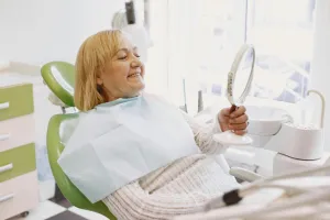Smiling patient admiring her smile in mirror after dental treatment