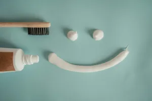 Toothbrush and toothpaste arranged into a smiley face on teal background